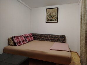 En säng med plats för en person, med ett mönstrat sänggavel, en inramad tavla på väggen och ett fönster med gardiner.