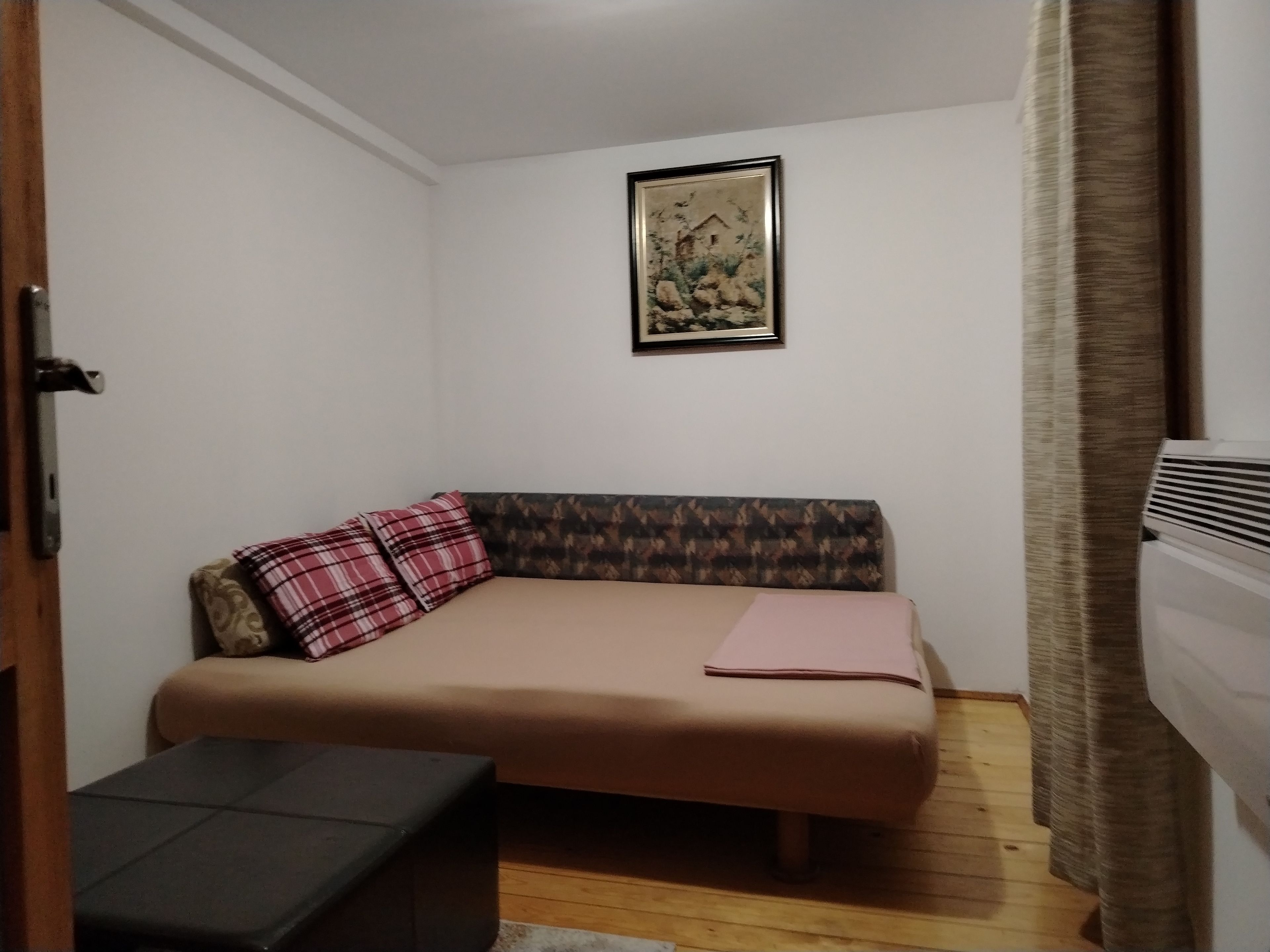 Una habitación pequeña con una cama individual, un banco, un cuadro enmarcado en la pared y un radiador.