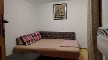 Una habitación pequeña con una cama individual, un banco, un cuadro enmarcado en la pared y un radiador.