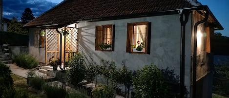 Ein zweigeschossiges Haus mit einem geneigten Dach, Holzläden und einem kleinen Garten.