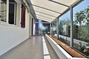 A corridor with a glass enclosure, a wooden bench, and a view of greenery outside. - Les Bruyères - à 700 m du port (La Richardais)