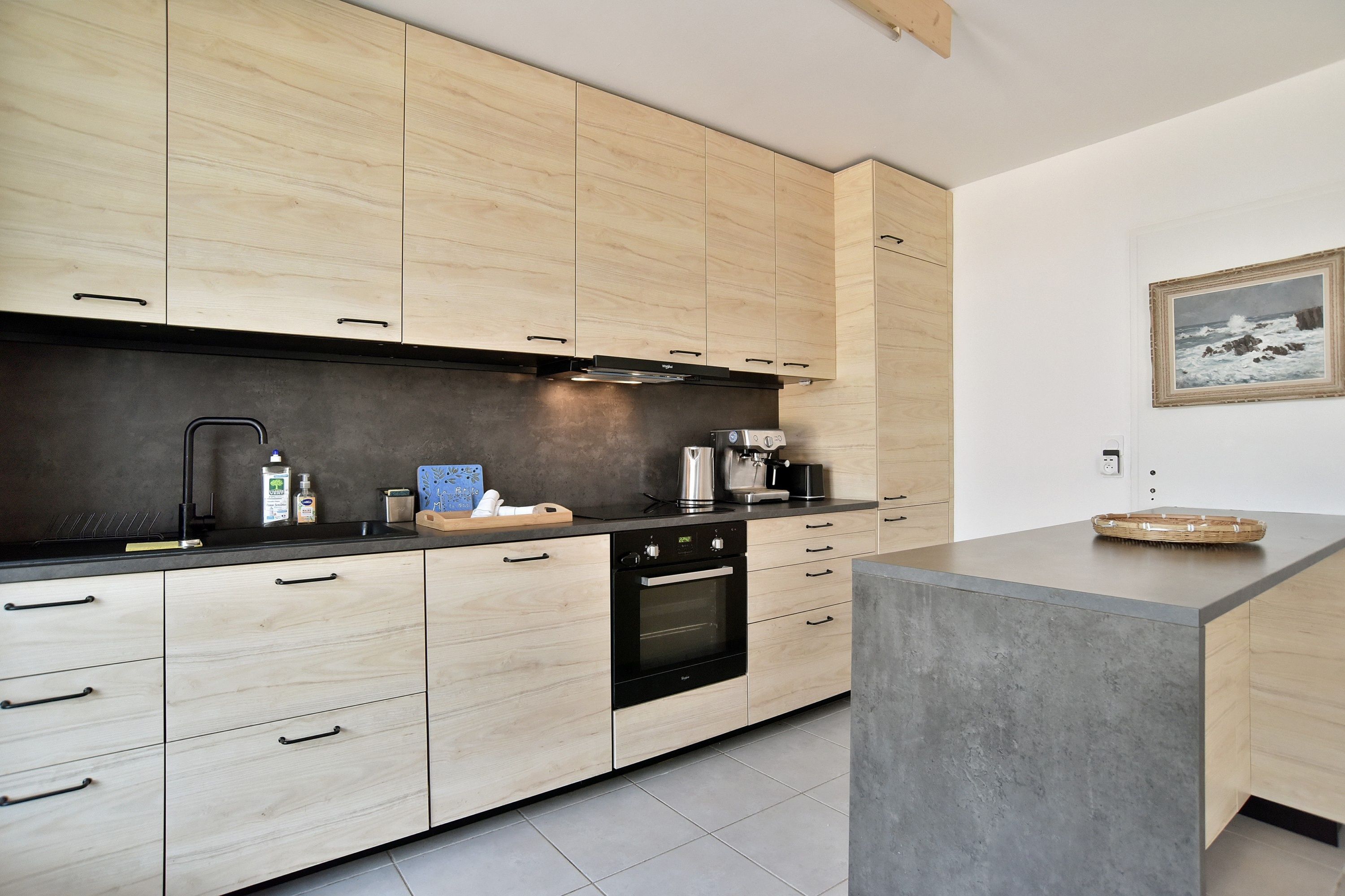 Una cocina moderna con armarios de madera clara, encimera negra y horno empotrado.