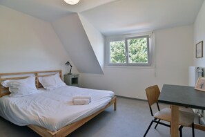 A bedroom with a bed, a desk, a chair, and a window with a view of trees. - Les Bruyères - à 700 m du port (La Richardais)