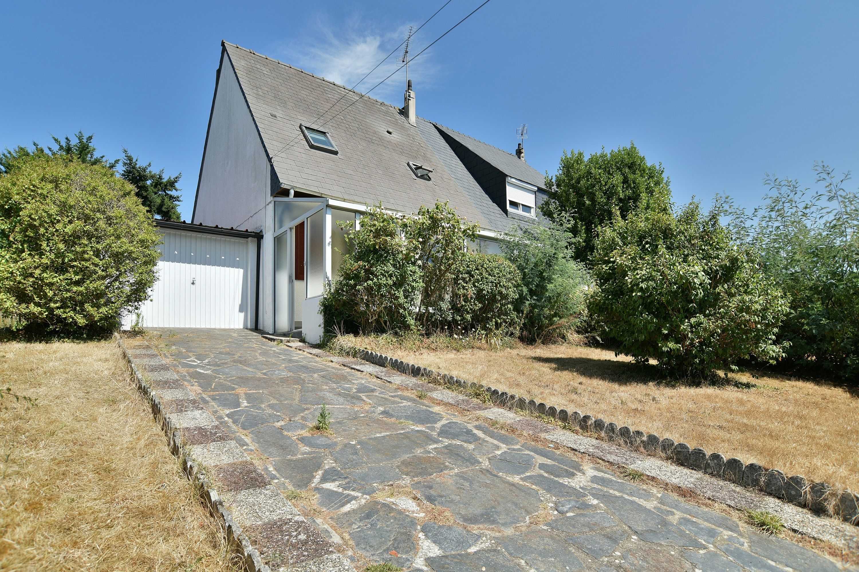 A house with a stone pathway leading to the entrance, surrounded by greenery.