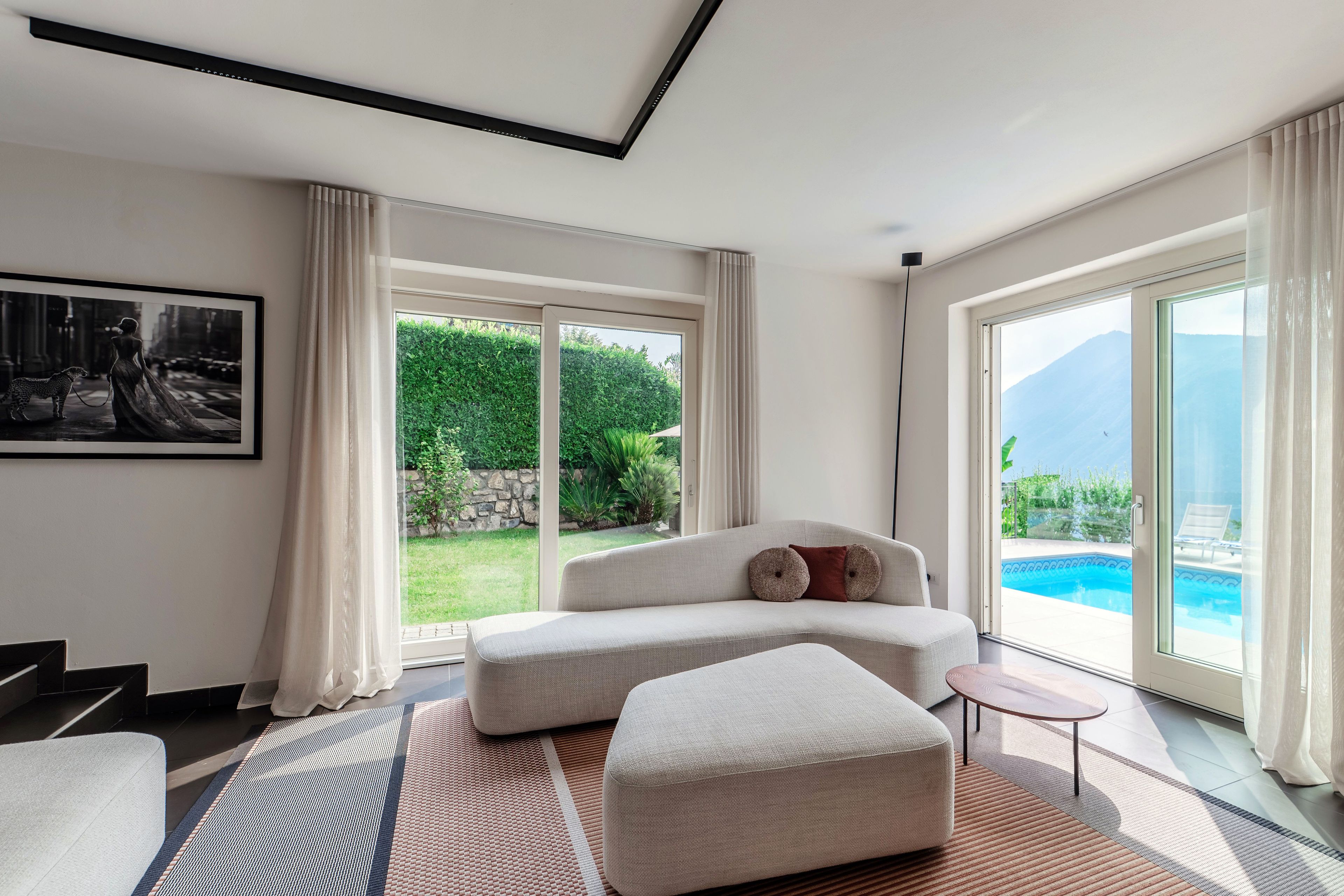 Ein modernes Wohnzimmer mit einer Couch, einem kleinen Tisch und Blick auf einen Swimmingpool.