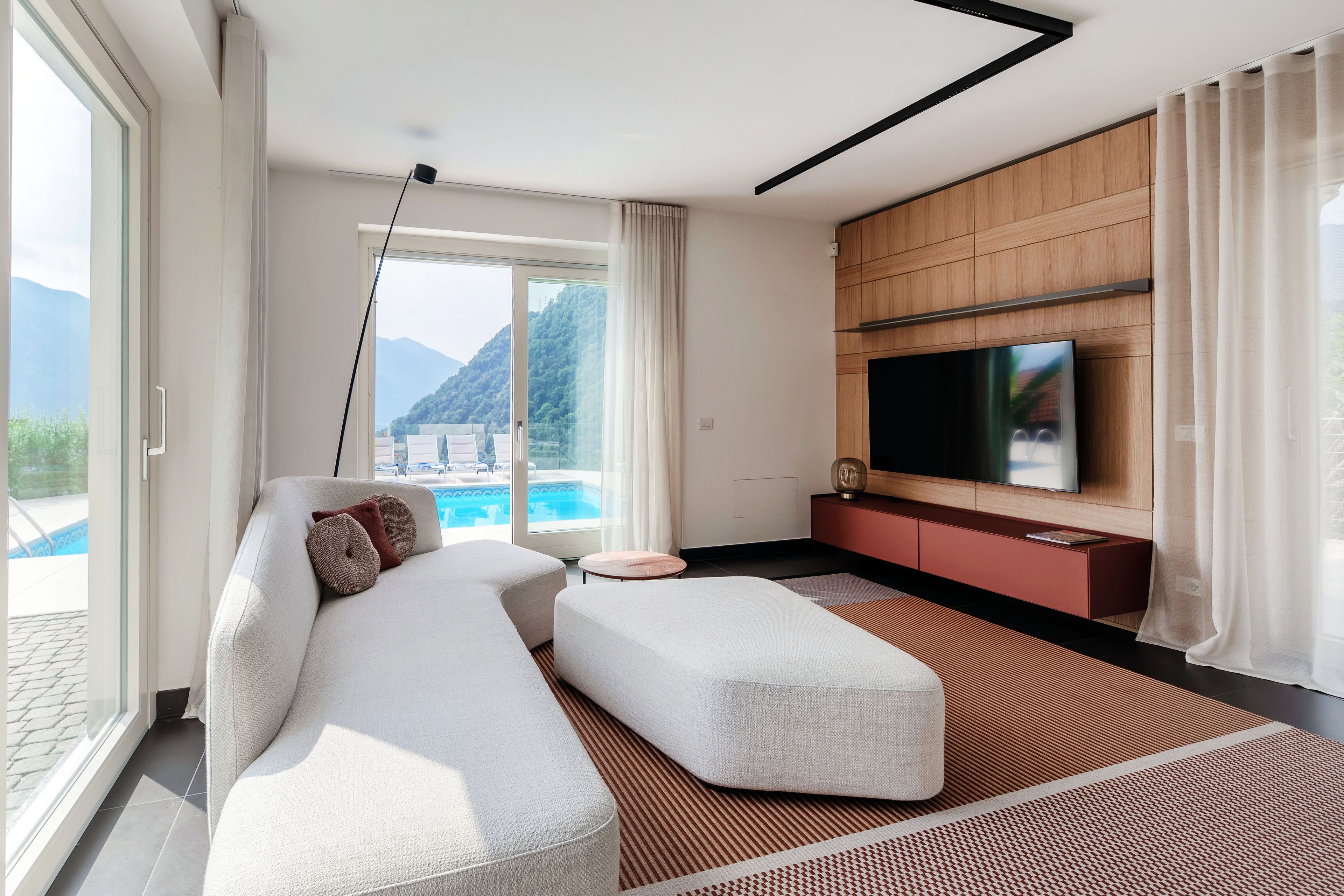 Ein modernes Wohnzimmer mit einer Couch, einem Hocker und einem Flachbildfernseher, der an einer Wand aus Holzpaneelen angebracht ist.