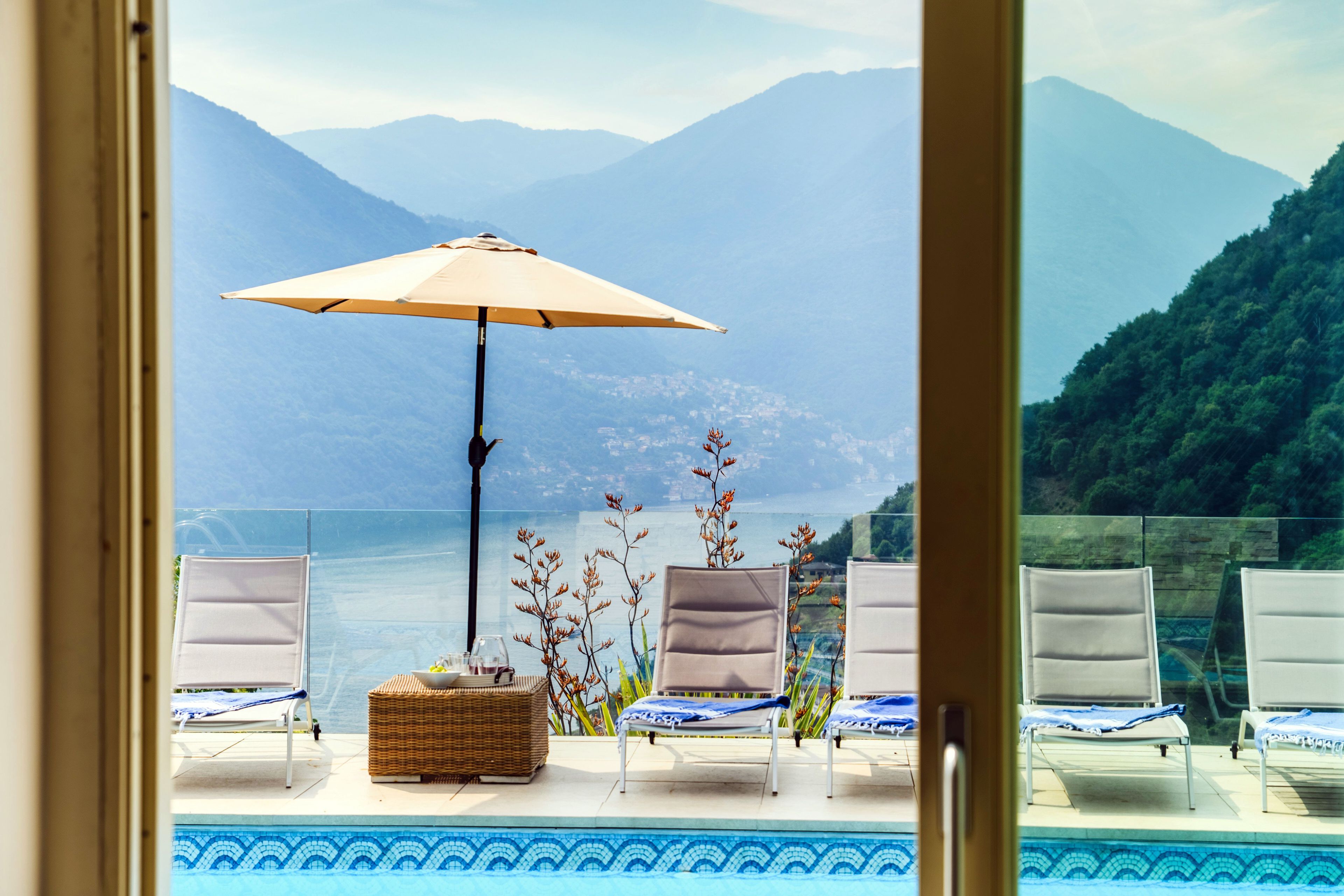 A poolside view with lounge chairs, an umbrella, and a view of mountains.