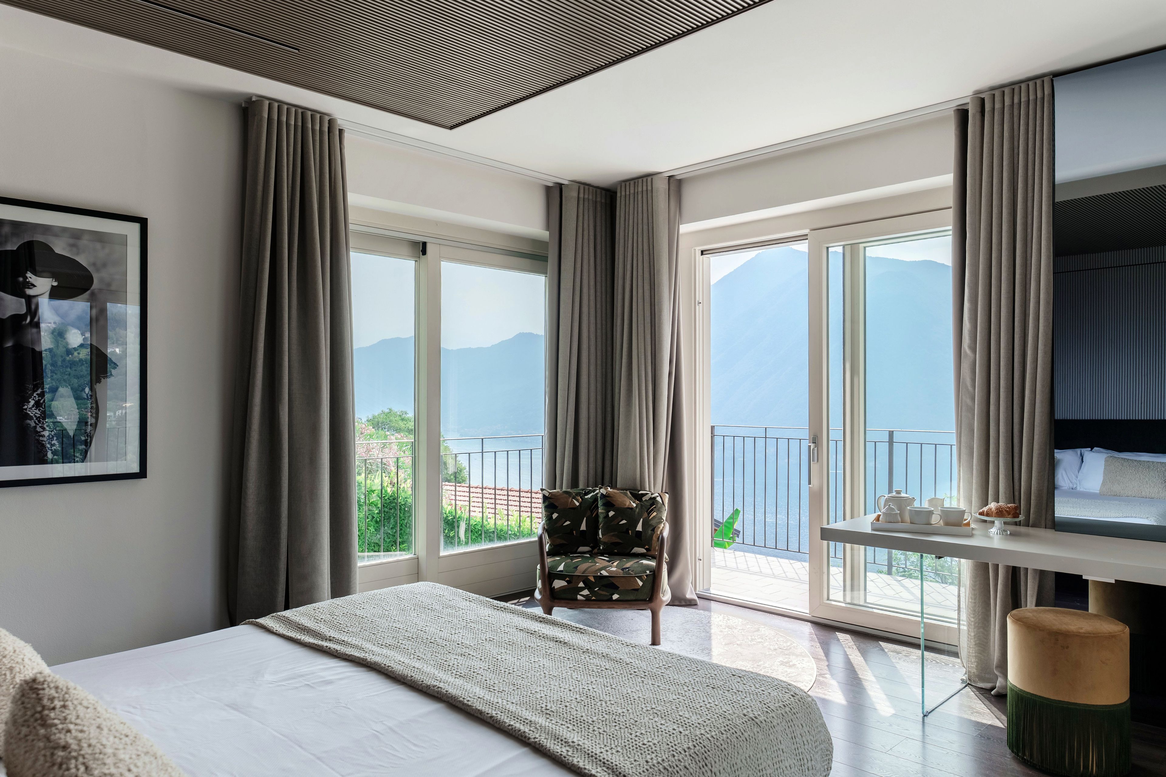 Ein modernes Hotelzimmer mit Bett, Sessel, Tisch mit Fernseher und großen Fenstern mit Bergblick.