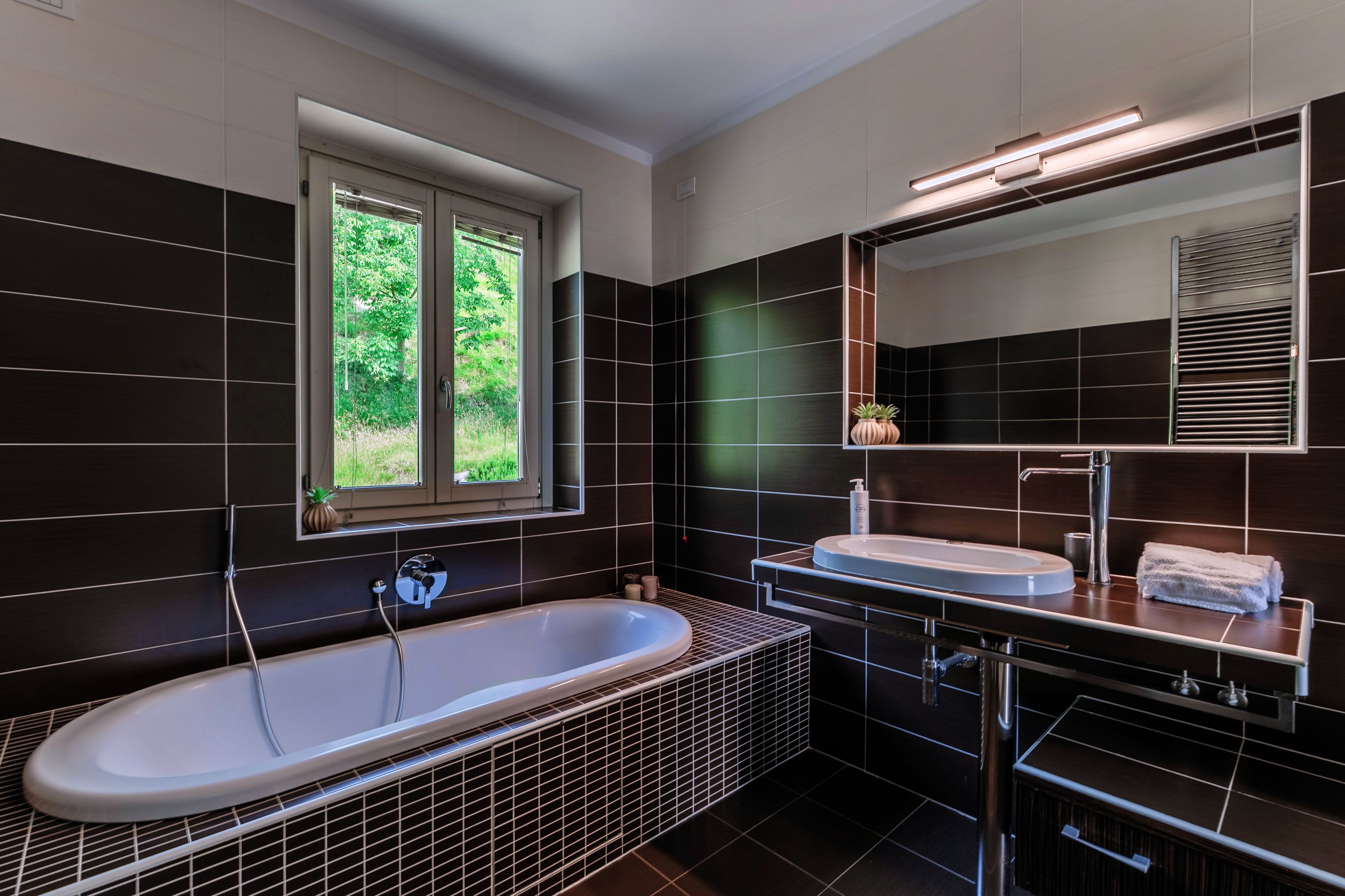 A modern bathroom with a freestanding bathtub, a vanity with a mirror, and a window providing a view of greenery.