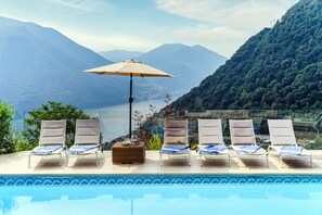 A poolside area with lounge chairs and an umbrella, overlooking a mountainous landscape. - Villa Lilla (Muronico)