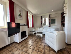 A living room with a fireplace, white sofas, a flat-screen TV, and a tiled floor. - Comfortable Heuvelland Family Escape (Gulpen)