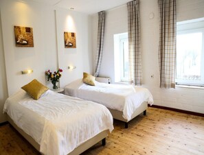 A hotel room with two beds, a window with curtains, and wall-mounted artwork. - Comfortable Heuvelland Family Escape (Gulpen)