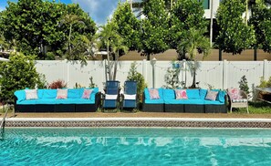 Un área junto a la piscina con una pileta de azulejos azules, una cerca blanca y una fila de sillas acolchadas en azul y blanco.