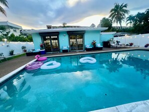 A swimming pool with inflatable rings, a patio area with outdoor furniture, and a building with large windows. - 3 min walk2 bch•Heat Pool•Bbq•100”TV•On Ocean Blvd (Fort Lauderdale)
