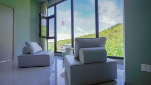 Una habitación moderna con dos sofás y una mesita, ventanas amplias con vistas a zonas verdes.
