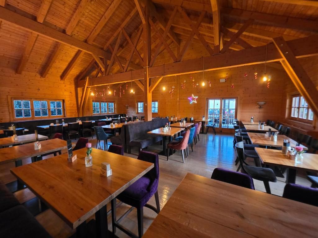 A spacious indoor dining area with wooden tables and chairs, high ceilings with exposed beams, and large windows allowing natural light.