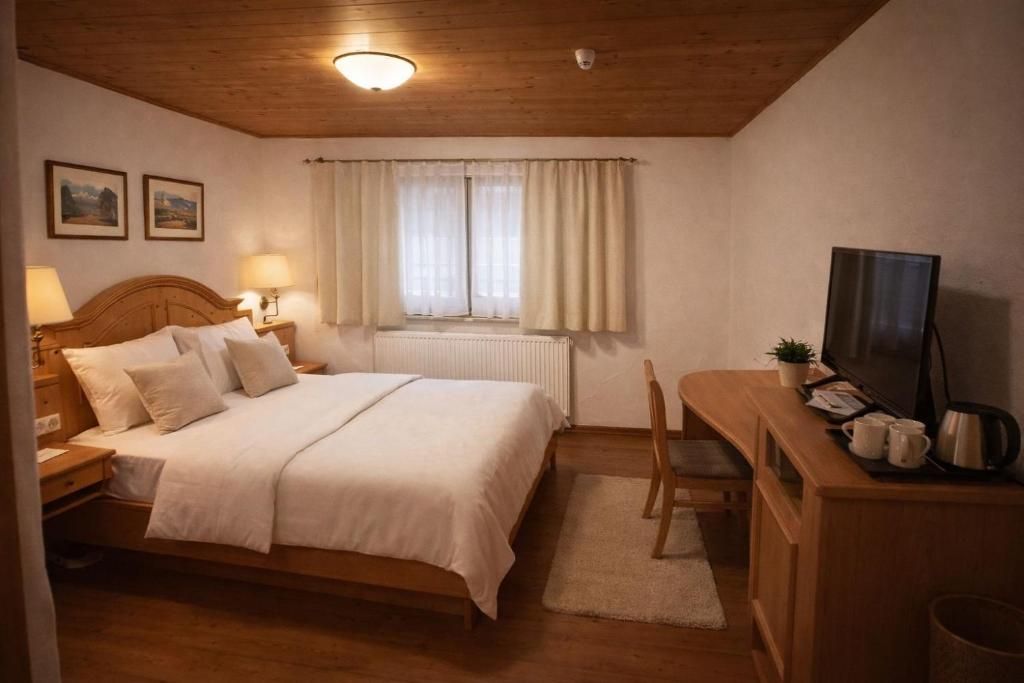 A bedroom with a wooden bed, bedside lamps, a desk with a television, and a window with curtains.