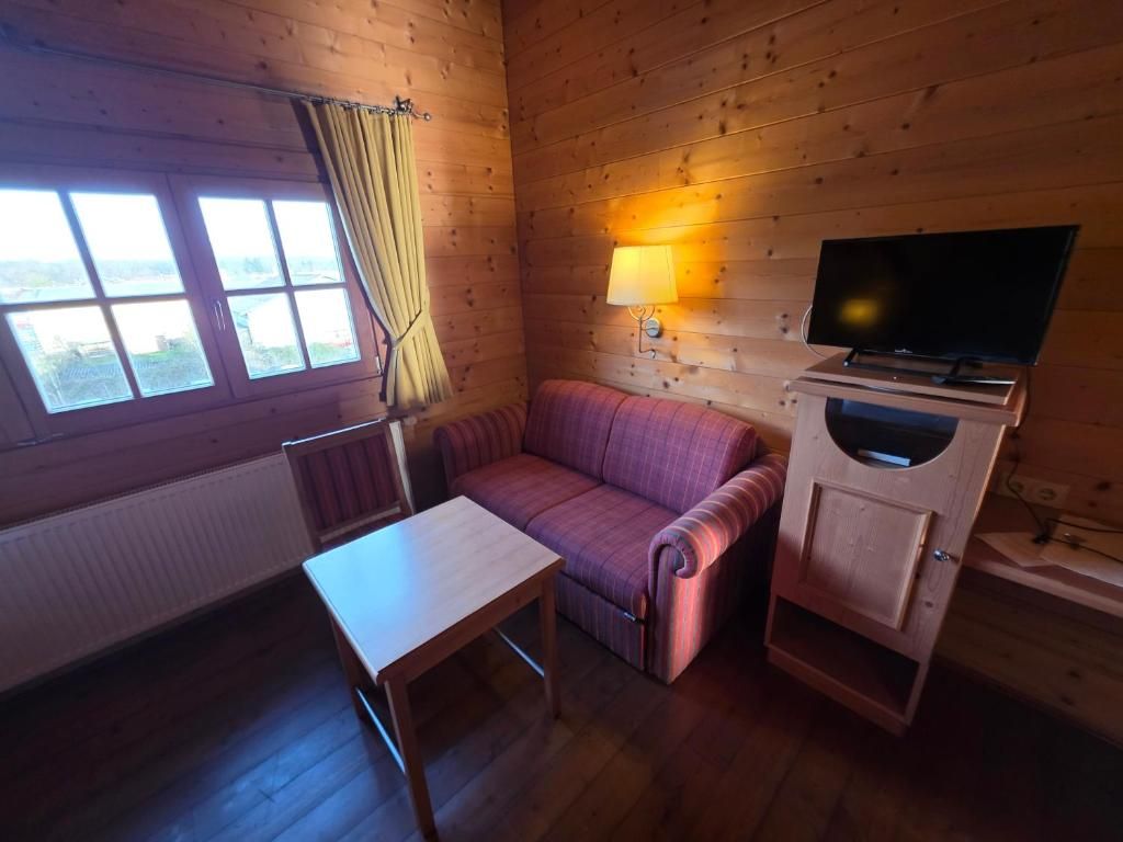 A cabin with a wooden interior, a sofa, a table, a lamp, and a television.