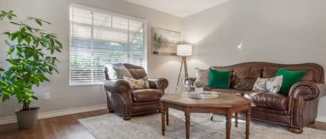 A living room with a brown leather sofa, a matching armchair, a coffee table, and a potted plant.
