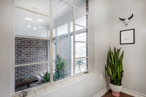 Ein Zimmer mit einem großen Fenster, einer Ziegelwand, einer Topfpflanze und einem gerahmten Bild an der Wand.
