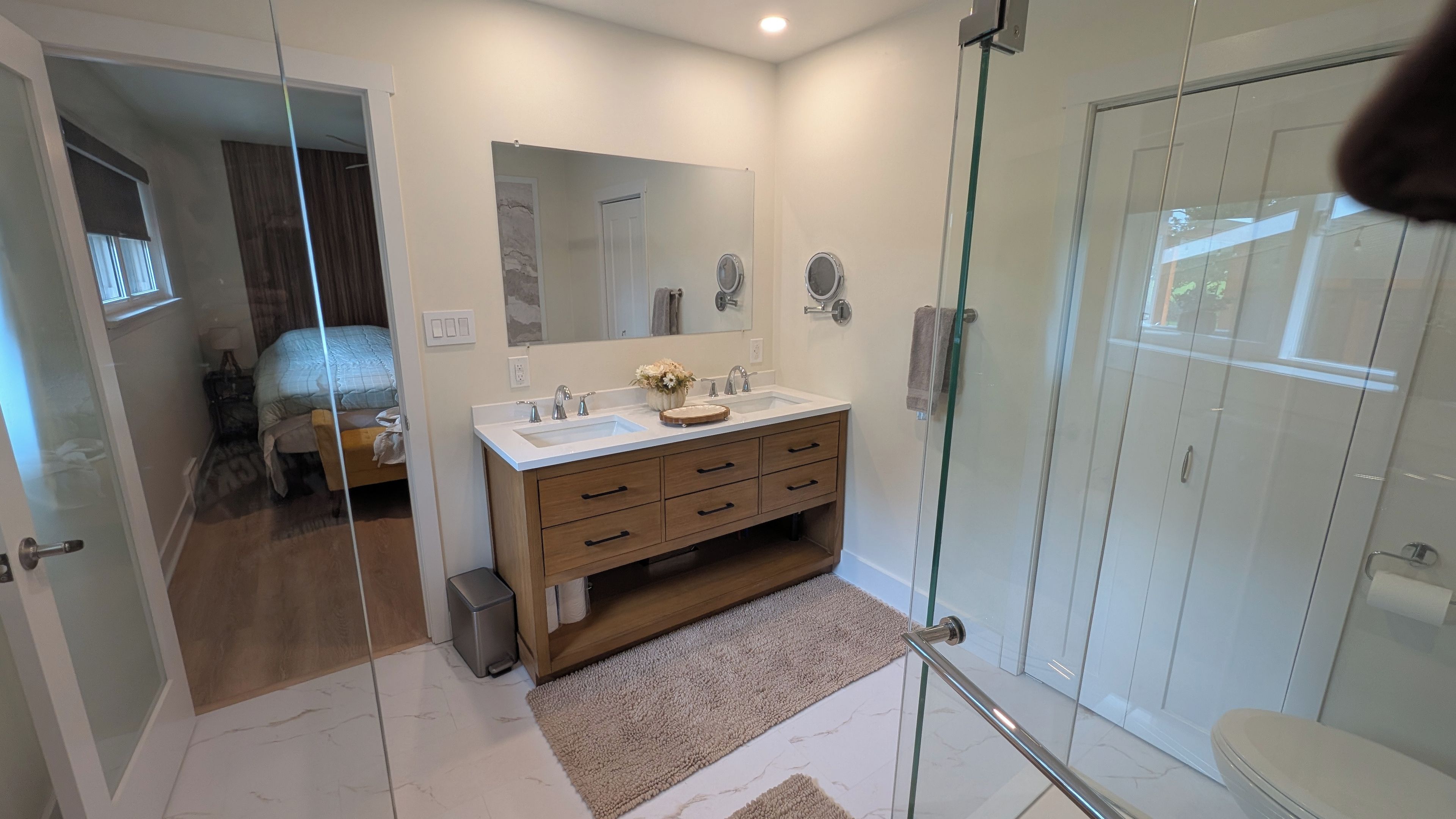 A modern bathroom with a glass shower enclosure, a wooden vanity, and a large mirror.