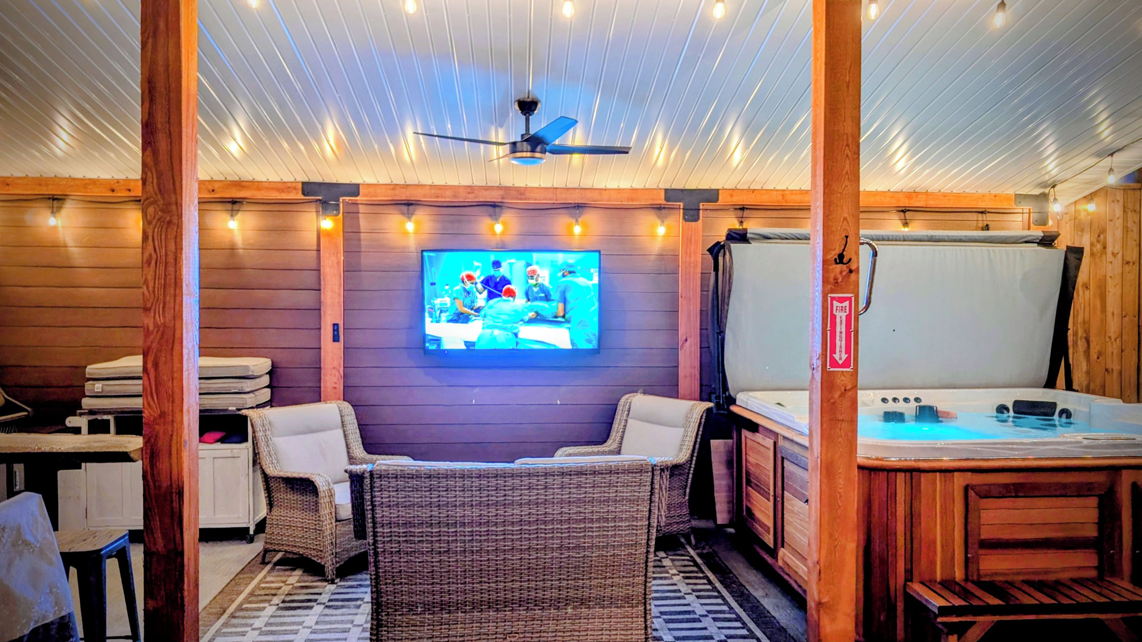 A room with a television, wicker furniture, a hot tub, and a ceiling fan.