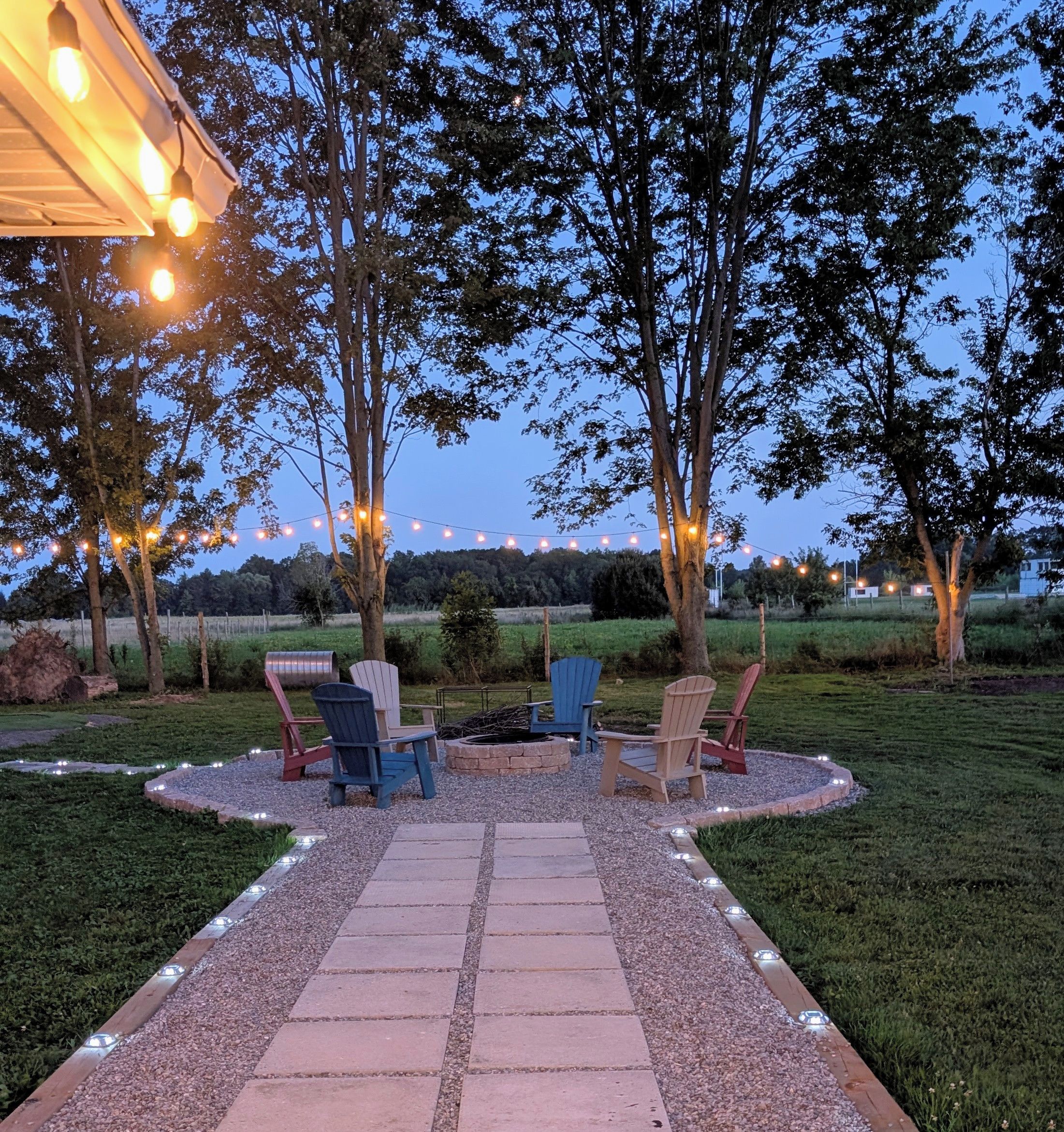 An outdoor seating area with chairs and a fire pit, surrounded by trees and a gravel path.