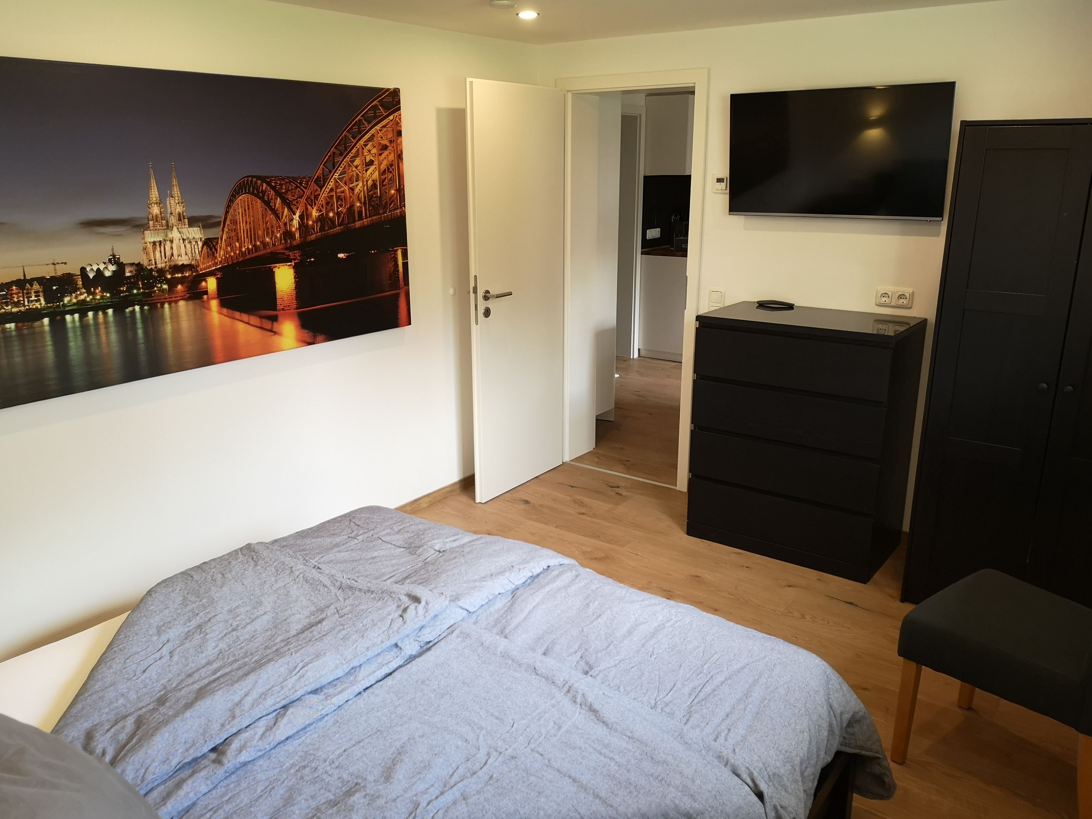Ein Schlafzimmer mit einem Bett, einem Schminktisch, einem Fernseher und einer Tür zu einem Flur.