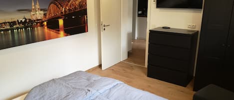 A bedroom with a bed, a dresser, a TV, and a door leading to a hallway.