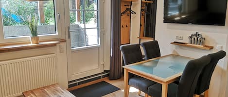 A modern room with a dining table, chairs, a TV, and a window with a view of greenery.