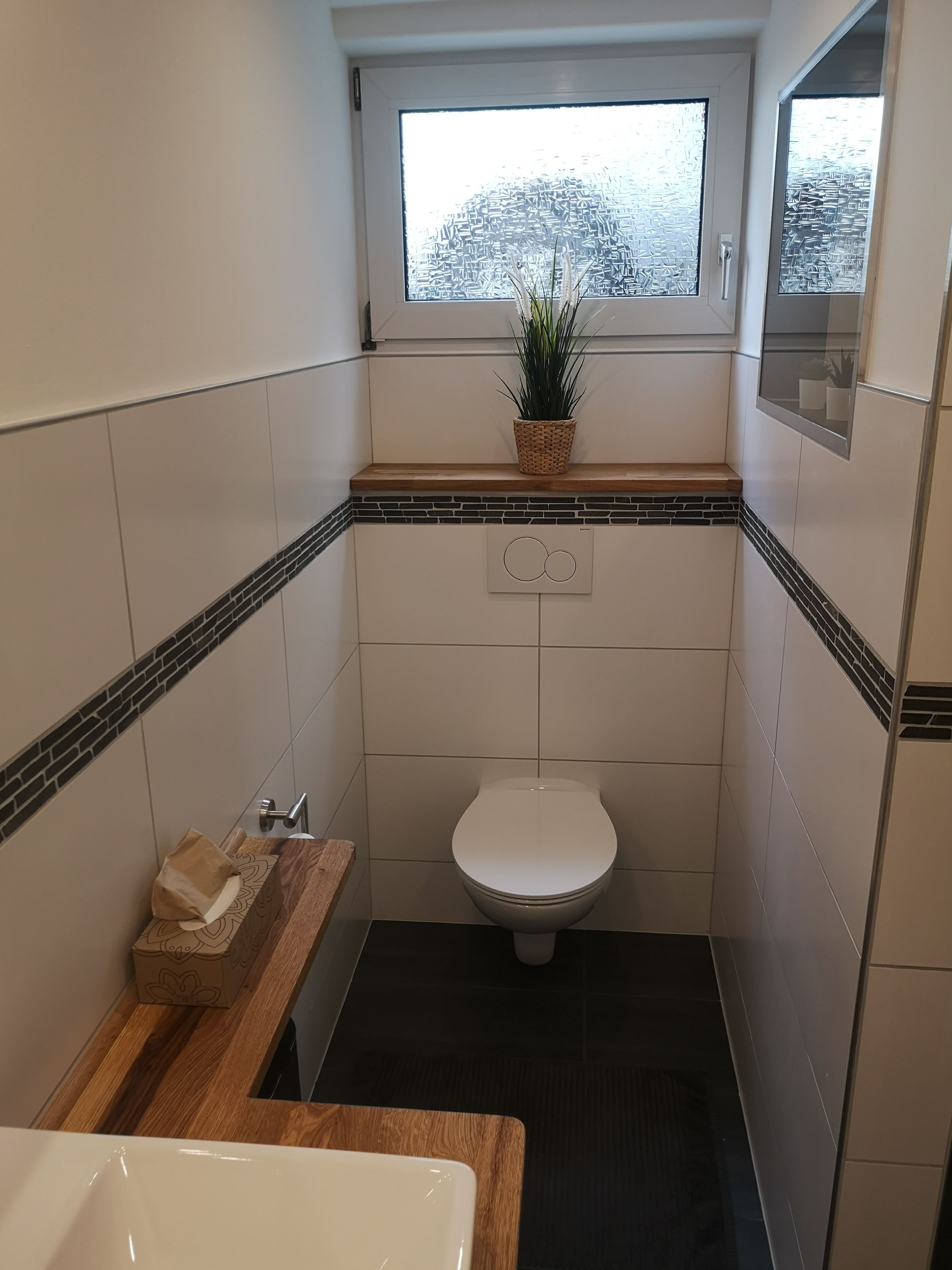 Ein kleines Badezimmer mit Toilette, einem Holzkosmetikschrank und einem Fenster mit einer Pflanze.