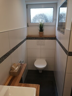 Ein kleines Badezimmer mit Toilette, einem Holzkosmetikschrank und einem Fenster mit einer Pflanze.