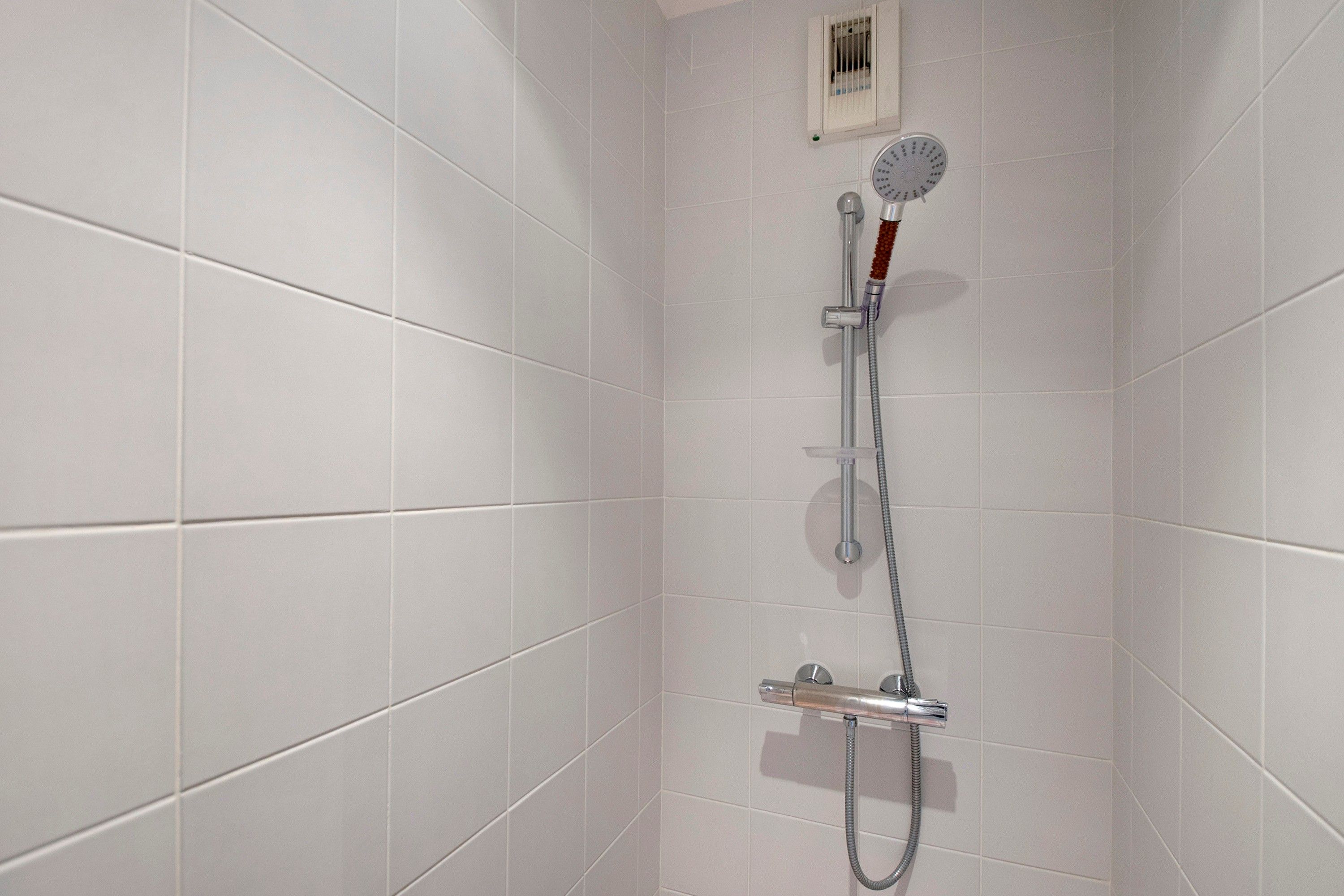 Ducha con cabezal de ducha manual y panel de control en la pared.