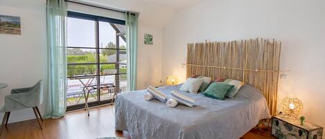 Ein Schlafzimmer mit einem Bett, einem Sessel, einem Fenster und Blick ins Freie.