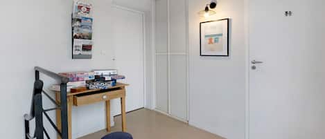 Un pasillo con una mesa de madera, un otoman azul, un cuadro enmarcado y una puerta blanca.