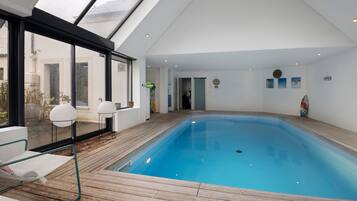 Una piscina interior con terraza de madera, ventanas amplias y vistas al exterior.