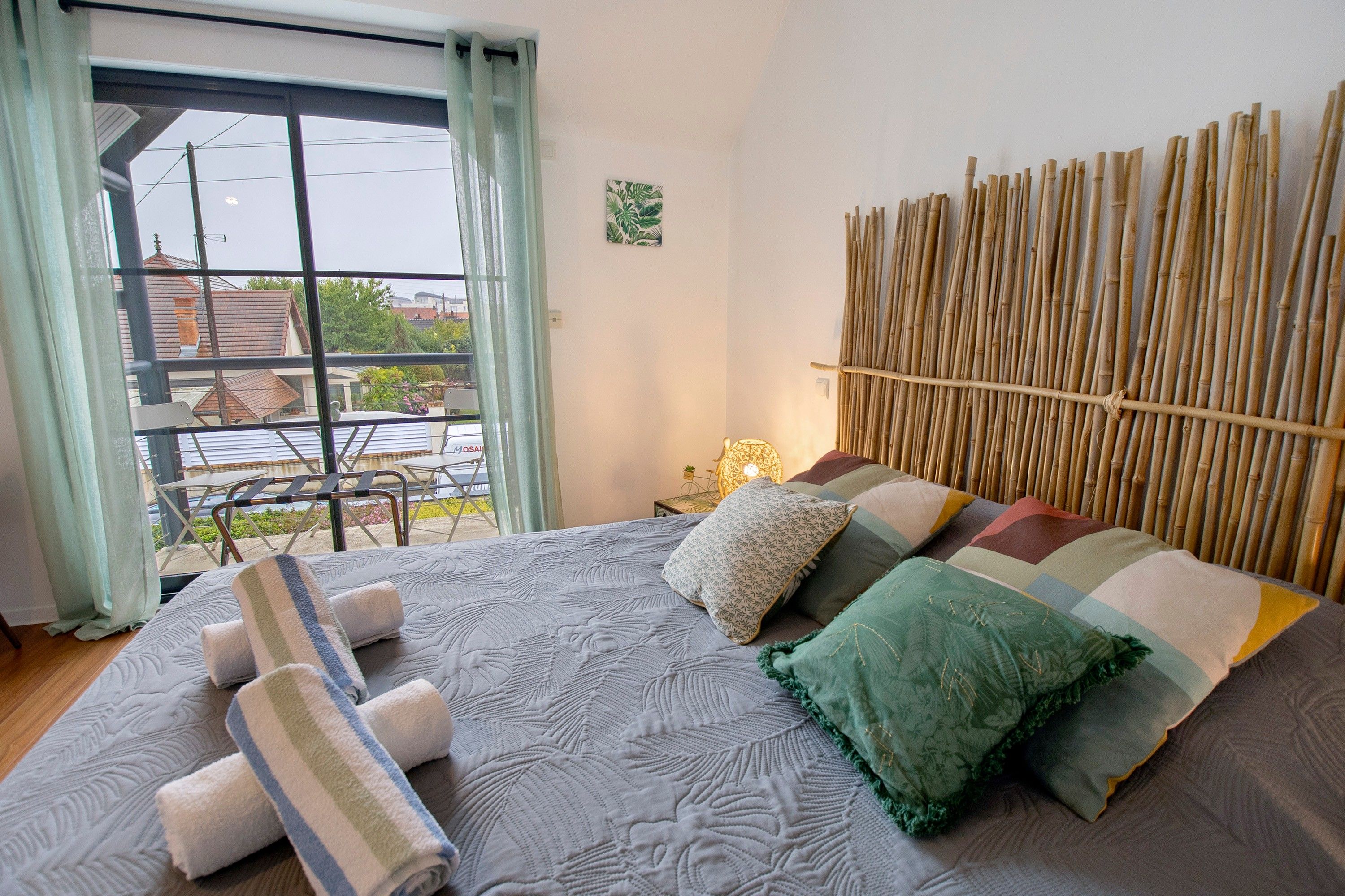 A bedroom with a bed, pillows, a window with curtains, and a view of the outside.