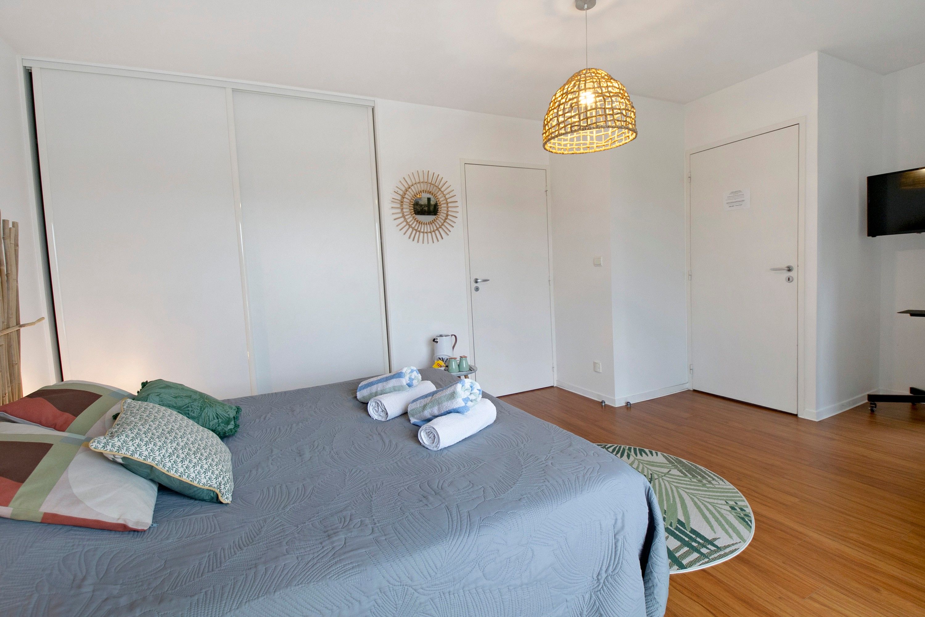 Une chambre à coucher comprenant un lit, un luminaire suspendu, un téléviseur et une porte ornée d’un miroir décoratif.