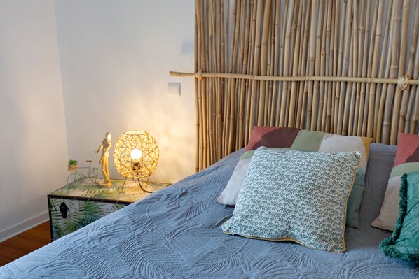 A bed with a patterned bedspread, a decorative lamp, and a bamboo wall.