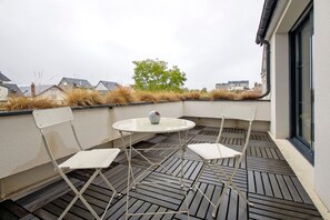 A small outdoor seating area with a round table and two chairs, a potted plant, and a view of the neighborhood.