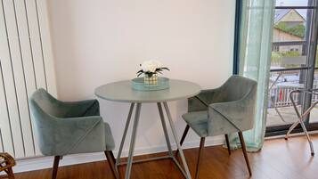 Una habitación con una mesa redonda, dos sillas, un jarrón con flores y vistas al exterior a través de una ventana.