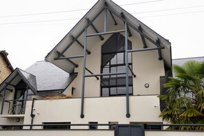A modern building with a triangular roof structure, large windows, and a visible balcony with outdoor furniture. - Bed and Breakfast 'Chambre Vue Sur Jardin' with Shared Terrace, Balcony and Wi-Fi (Caen)