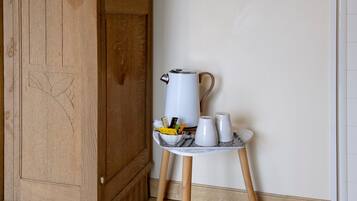 Una tetera blanca sobre un soporte de madera, junto a tazas y un cuenco pequeño con bolsitas de té y una cuchara.