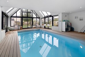 Una piscina interior moderna con un deck de madera, ventanas grandes y vistas al exterior.