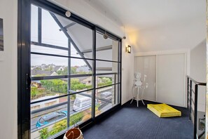 A room with a large window, a yellow mattress, and a white chair.