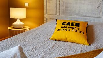 A bed with a patterned bedspread, a yellow pillow with text, a bedside lamp, and a wall with carved designs.