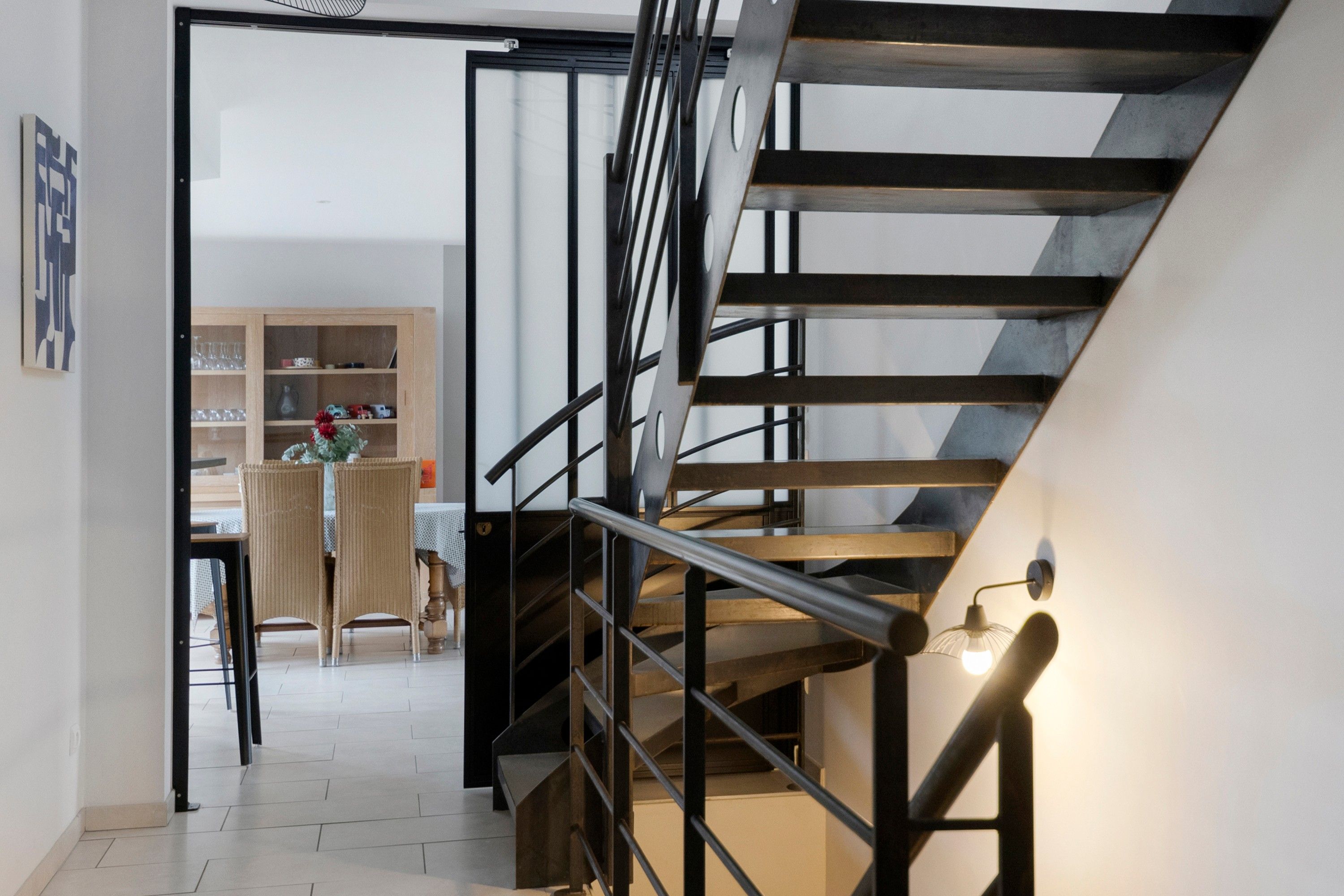 A modern interior with a staircase, a dining area, and a bookshelf.