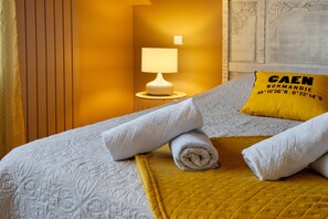 A neatly made bed with rolled towels, a yellow throw blanket, and a pillow with text.