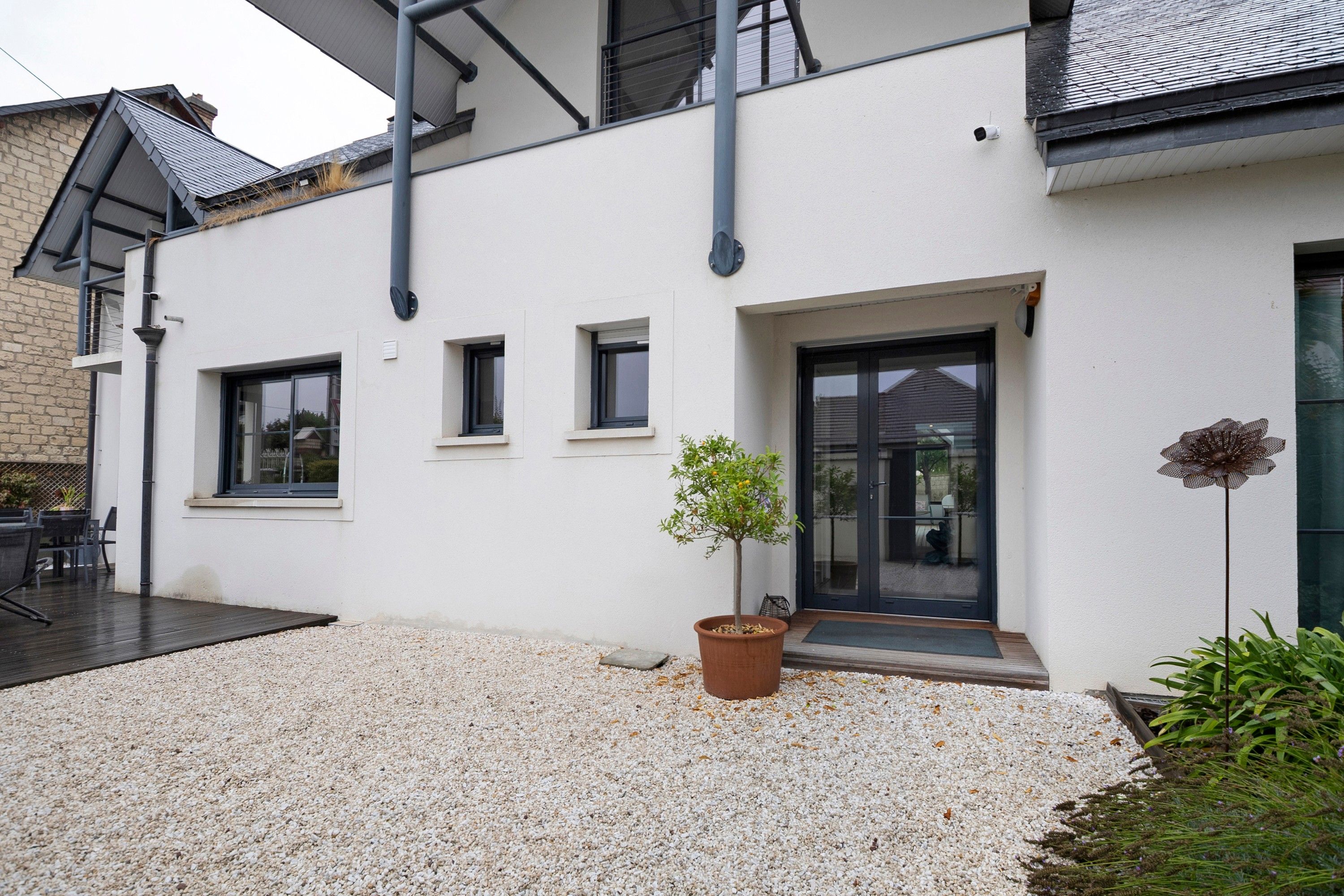 Un bâtiment moderne à l’extérieur blanc, avec une allée en gravier et un pot de fleurs.