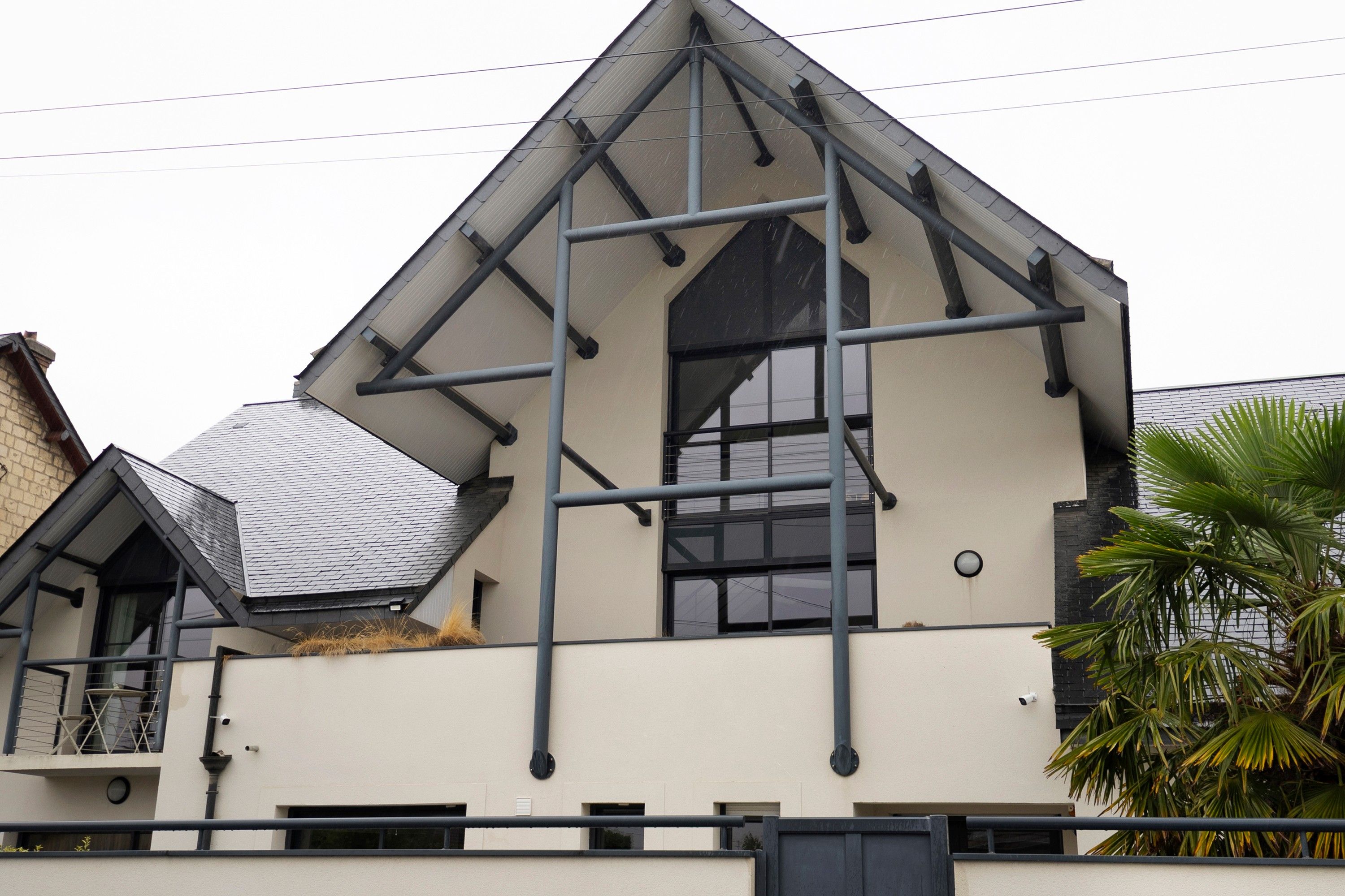 Un bâtiment moderne doté d’une structure de toit triangulaire, de grandes fenêtres et d’un balcon bien visible, aménagé avec du mobilier d’extérieur.